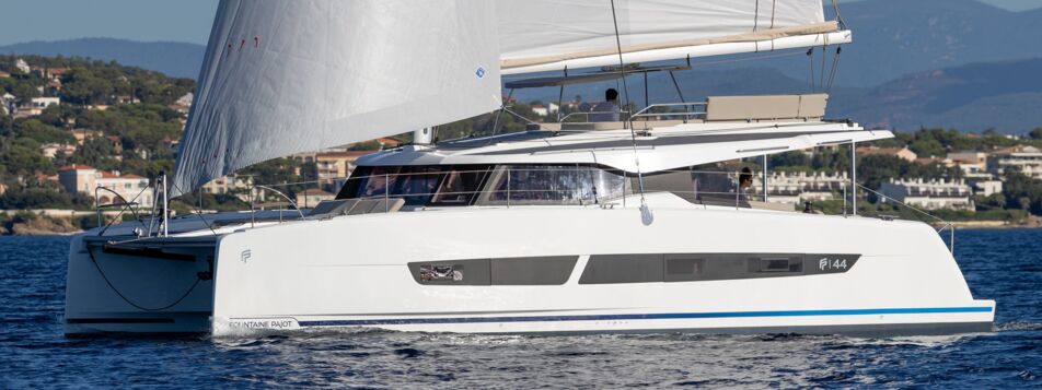Seitenansicht eines Fountaine Pajot FP 44 Katamarans unter vollen Segeln vor bergiger Küste – Yachtcharter Mallorca