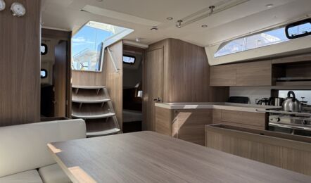 Perspektive vom Salontisch im Salon der Segelyacht Oceanis 47 „Große Freiheit“ mit dunklem Holzausbau und offener Pantry – Yachtcharter Ostsee