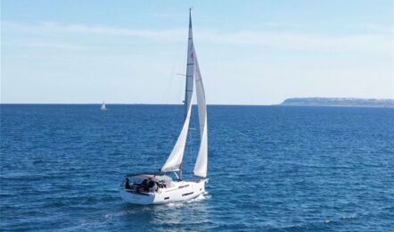 Die Segelyacht Hanse 460 „Antares“ segelt auf offenem Meer vor einer Landzunge – Yachtcharter Mallorca