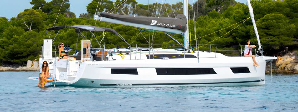 Seitenansicht einer Dufour 44 mit Bimini und Badeplattform vor Anker (Werftbild) – Yachtcharter Mallorca