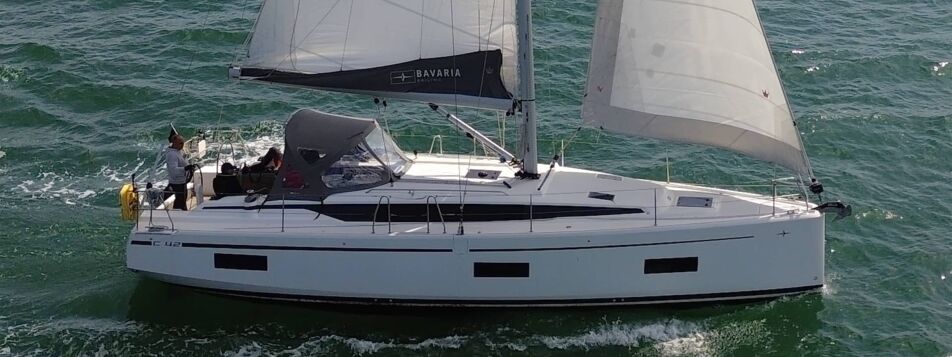 Bavaria C42 „Chapeau“ unter vollen Segeln mit Bimini und Crew im Cockpit auf der Ostsee – Yachtcharter Heiligenhafen