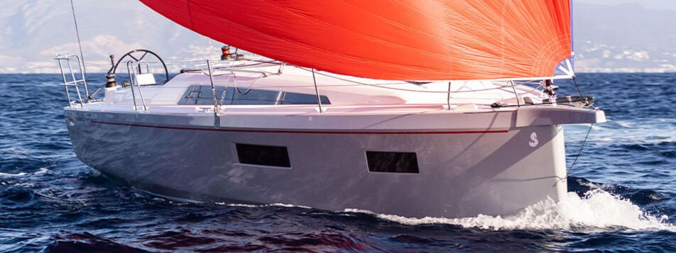 Eine Segelyacht Oceanis 34.1.2 segelt unter rotem Gennaker vor Küstenkulisse (Werftbild) – Yachtcharter Ostsee