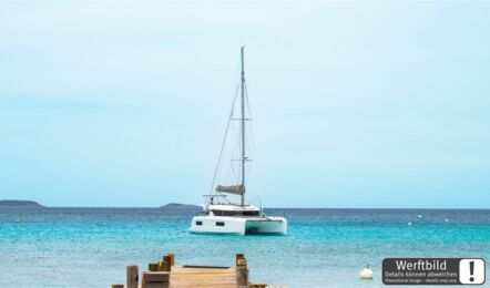 Steuerbordansicht einer Lagoon 38 am Bug vor Anker in einer Bucht mit Blick auf das Schiff aus der Ferne (Werftbild) – Yachtcharter Mallorca