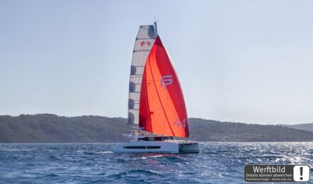Ein FP 44 Katamaran segelt mit rotem Gennaker und FP-Logo vor grüner Küste (Werftbild) – Katamarancharter Mallorca