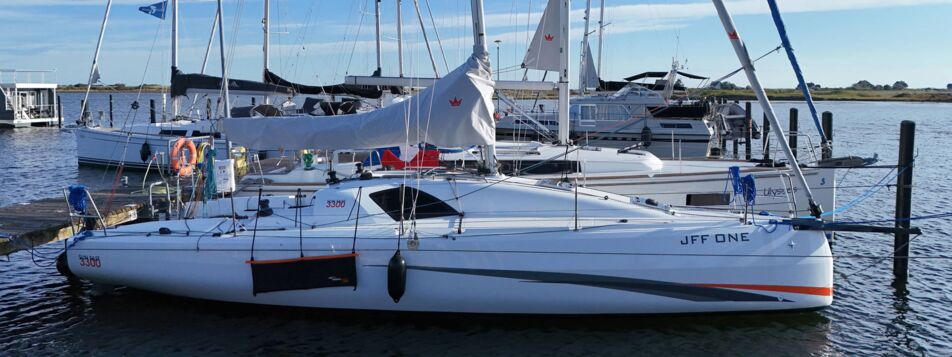 Längsseits am Steg liegende Segelyacht Sun Fast 3300 „JFF One“ mit Namenszug am Rumpf in Heiligenhafen – Yachtcharter Ostsee